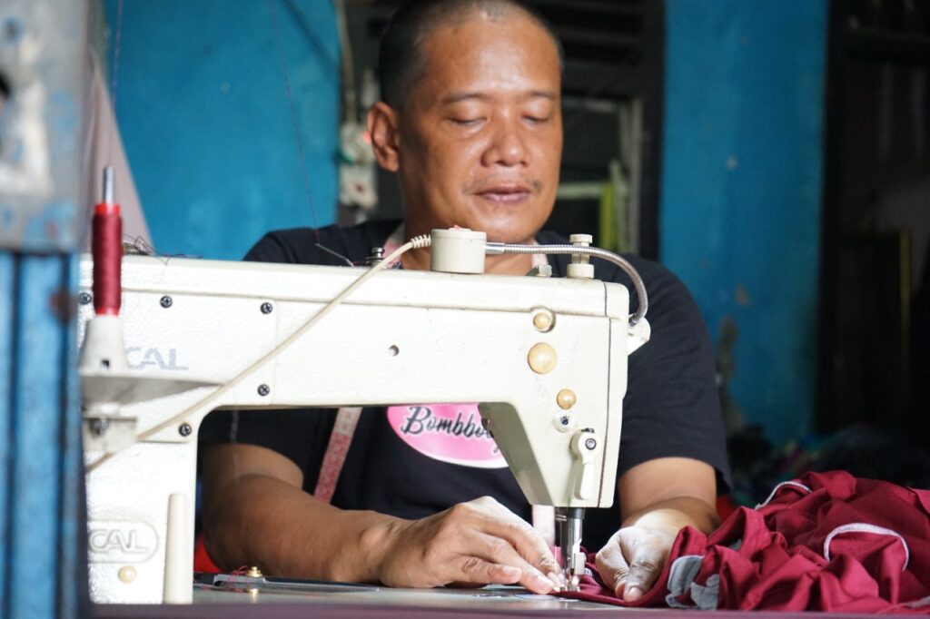 photo20220224120742 dompet dhuafa A textile worker guiding red fabric through a vintage sewing machine, focused on stitching.