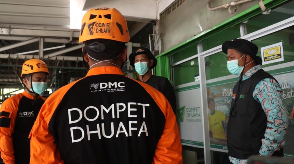 Rescue workers in orange uniforms and helmets with masks stand indoors, Dompet Dhuafa DMC logo visible on jackets.