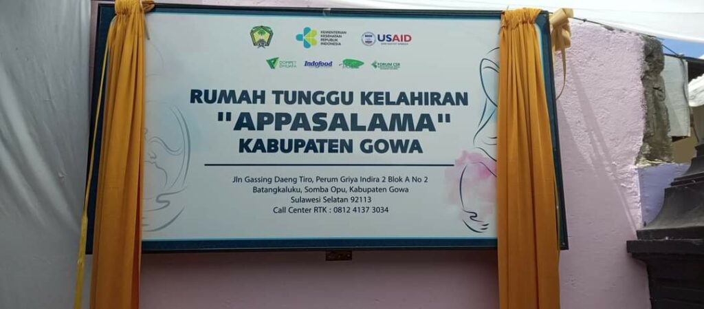 photo202203141227541 dompet dhuafa Signboard banner for 'Rumah Tunggu Kelahiran Appasalama' in Kabupaten Gowa, with logos and yellow curtains framing the display.