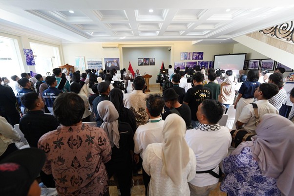 peringatanharinakbake783 dompet dhuafa Large group of people standing in a conference room, facing a panel at the front with flags and a projector screen, suggesting a formal event or ceremony.