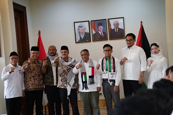 peringatanharinakbake788 dompet dhuafa Group of men and a woman posing indoors, several wearing keffiyehs, raising fists in solidarity, with a Palestinian flag and portraits on the wall behind them.