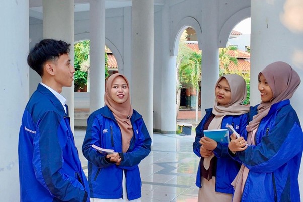 radha heryani putri 6 dompet dhuafa Four students in blue jackets stand in a colonnade courtyard, chatting and holding notebooks.