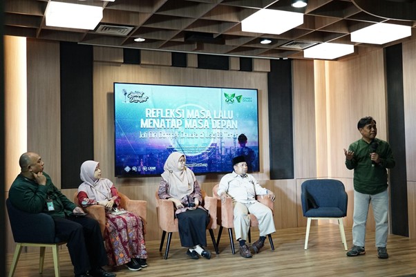 refleksi jati diri 9 dompet dhuafa Panel discussion in a room with five people seated on stage and a presenter standing to the right, a large screen behind displays Indonesian text about reflecting on the past and future.