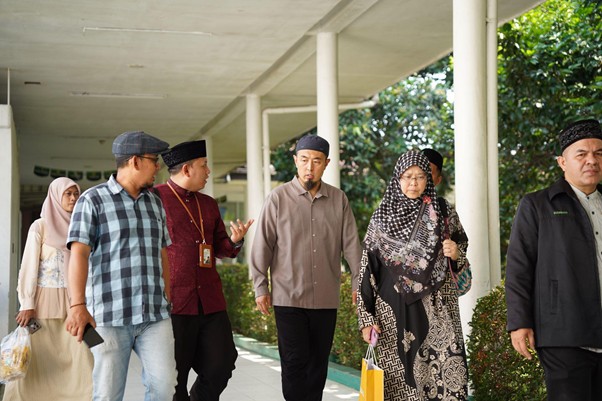 sensei sugimoto kunjungi smart 10 dompet dhuafa Group of six adults walking together along a shaded walkway; some wear traditional Muslim clothing and hijabs, outdoors near a building.
