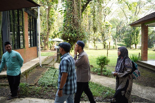 sensei sugimoto kunjungi smart 4 dompet dhuafa A group of four adults walk along a path between brick buildings in a green park area, engaged in conversation.
