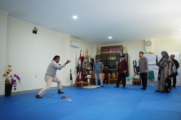 sensei sugimoto kunjungi smart 6 dompet dhuafa Instructor demonstrates a martial arts move on blue mats as students watch in a dojo full of trophies and equipment behind them.