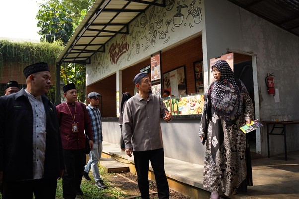 sensei sugimoto kunjungi smart 8 dompet dhuafa Group of men in traditional caps listen to a woman in a patterned hijab speaking near an outdoor food stall.
