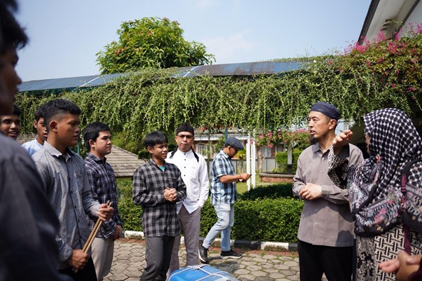 sensei ke smart 1 dompet dhuafa Group of young men and women standing in a semicircle outdoors, listening to a man in a cap who seems to be teaching.