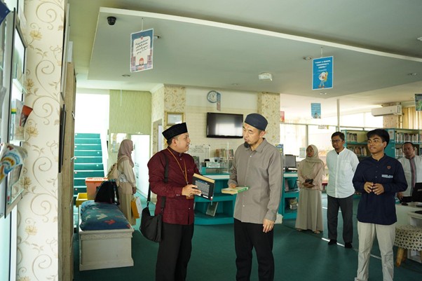 Two men wearing traditional hats converse in a bright, teal-carpeted lobby while others stand in line in the background.