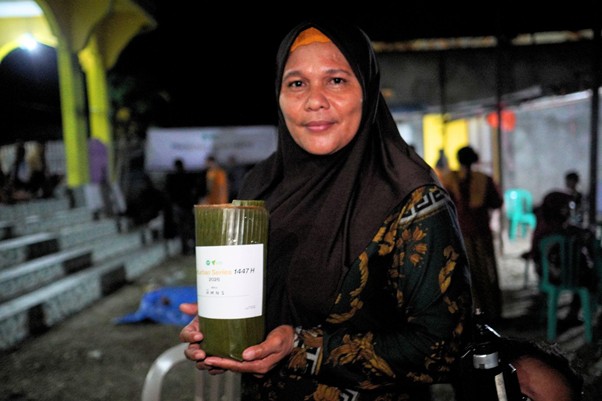 Woman in a black hijab at night holding a green, bamboo-wrapped package with a white label.