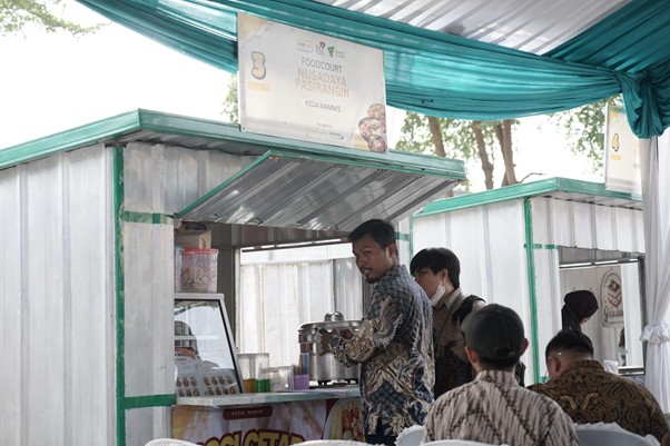 umkm cileungsi 3 dompet dhuafa Outdoor food stall with teal canopy; a man serves customers at the counter while others wait, sign above reads 'Food Court Nusadaya Pasirangan'.