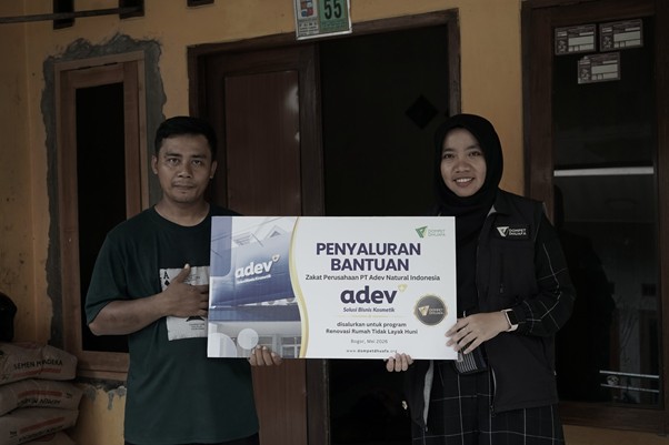 zakatptadev5 dompet dhuafa Two people stand outside a doorway, holding a large sign that reads 'Penyaluran Bantuan' for a donation program (charity context).