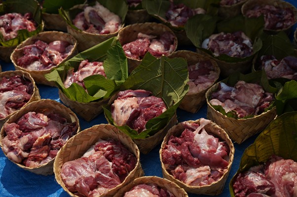 pertumbuhan thk 2026 11 dompet dhuafa Multiple woven baskets filled with raw pork cuts on a blue cloth, with green leaves scattered around.