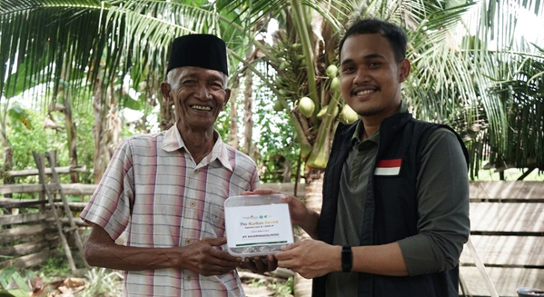 pertumbuhan thk 2026 15 dompet dhuafa Two men stand outdoors among palm trees; an old man in a checkered shirt and cap receives a certificate from a younger man in a black vest, both smiling.