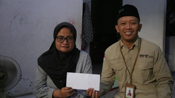 Woman in a hijab holds a white envelope while a smiling man in a khaki uniform sits beside her.