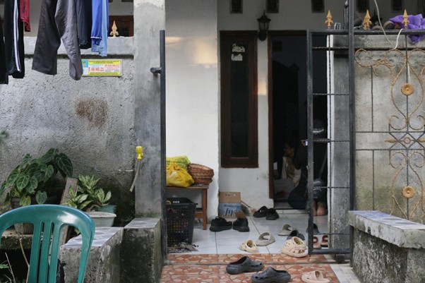 Open gate to a small home with shoes scattered on the tiled floor and clothes drying above, a person inside by the doorway.