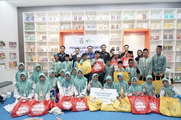 Group of volunteers posing after a donation drive, with many colorful bags labeled for distribution in a room with shelves and a banner behind them.