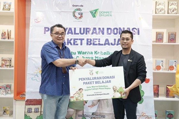 besteam gramedia 9 dompet dhuafa Two men shake hands while presenting a sign about donating study packages at an educational charity event, standing in front of a banner with logos in a bookstore setting.