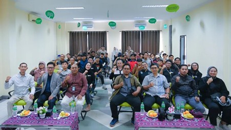 Group of attendees in a bright conference room posing for a photo, front tables with fruit and drinks, green balloons overhead at a workshop.