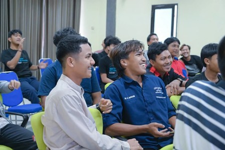 Group of young men seated in colorful chairs in a bright room, smiling and chatting during a workshop or training session.