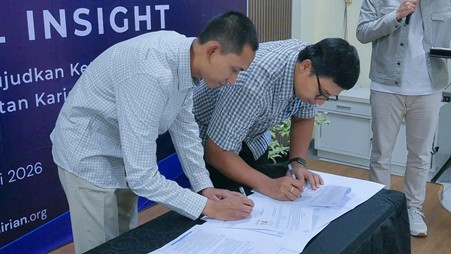 Two men in checkered shirts sign documents on a table at an event, with a blue banner in the background reading 'INSIGHT' and others partially visible.