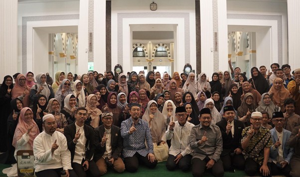Large diverse group posing for a group photo in an ornate hall, many attendees raising one finger in a gesture of unity.