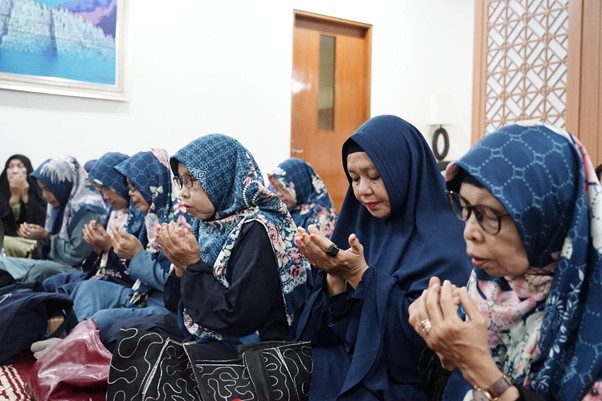 Group of women in blue hijabs sitting on the floor, cupping their hands in prayer.
