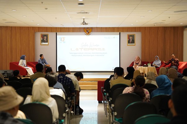 Panel discussion in a conference room with speakers on stage and an audience watching a presentation on a screen in the center.