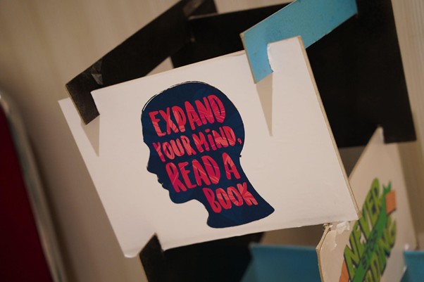 gelar wicara 10th sli 4 dompet dhuafa Poster card with a blue head silhouette and pink slogan: 'Expand your mind. Read a book', taped to a display surface.