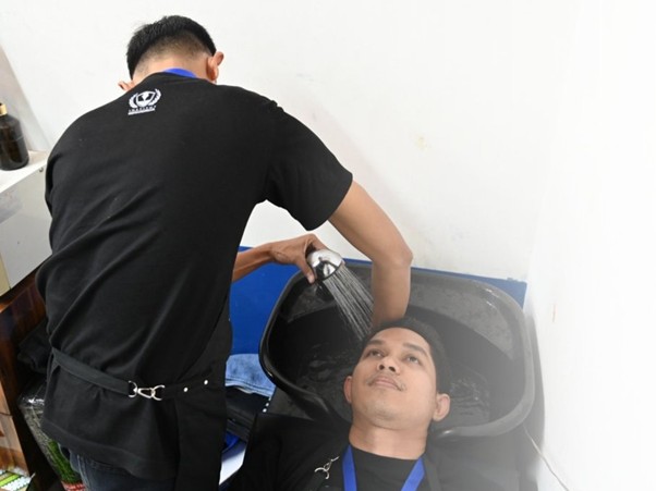 industribarberinstitutkemandirian2 dompet dhuafa Man getting his hair washed at a salon sink while a stylist rinses his hair over a shampoo basin.