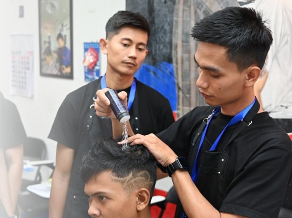 industri barber institut kemandirian 7 dompet dhuafa Barber sprays styling product onto a client's hair while another barber watches in a salon.