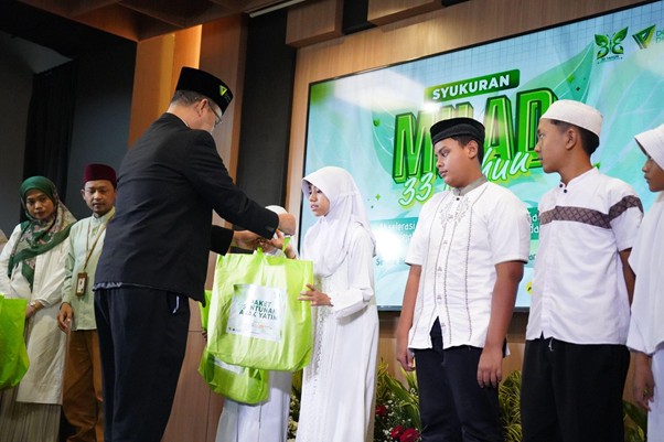 milad 33 th dompet dhuafa 4 dompet dhuafa Man in a dark suit hands a green gift bag to a girl in a white hijab on a stage during a ceremony.