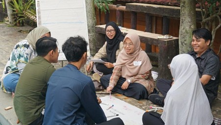 ngobrol bumi 2026 2 dompet dhuafa Group of eight adults sitting in a circle outdoors, collaborating over papers on a large sheet on the ground.