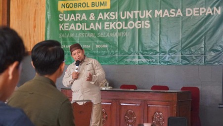 ngobrolbumi20264 dompet dhuafa Speaker in a beige shirt addresses an audience at a wooden podium during an ecological justice event, green banner in Indonesian behind him.