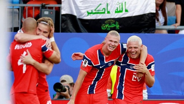 norwegia vs israel 4 dompet dhuafa Two red-uniform athletes hug and celebrate on a sports court, a flag with green Arabic text waving behind them.