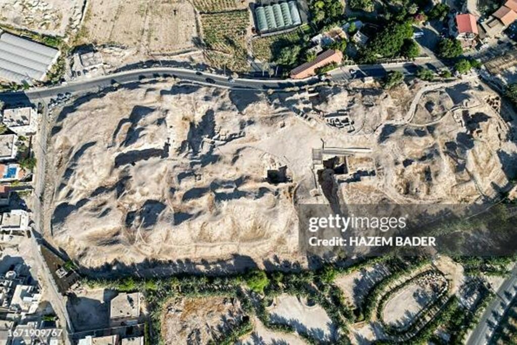 Aerial view of an archaeological excavation on a rocky hillside with terraces, roads, and nearby buildings.