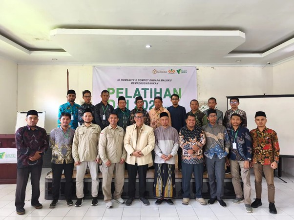 Group of men posing for a training workshop photo in a bright indoor room, with a banner that reads 'PELATIHAN' behind them.