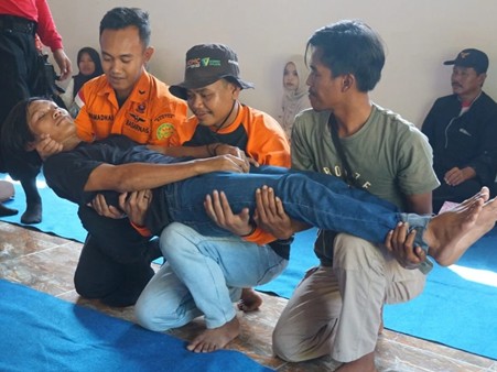 pelatihanbencanadmcdilebak3 dompet dhuafa Rescue workers carry an injured person on a blue mat, with two supporters at the torso and head and another at the legs, while onlookers watch.