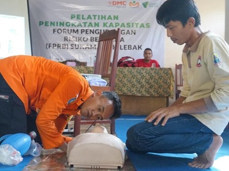 pelatihanbencanadmcdilebak4 dompet dhuafa Two men participate in CPR training, practicing on a manikin during a workshop in a hall with a banner in the background.