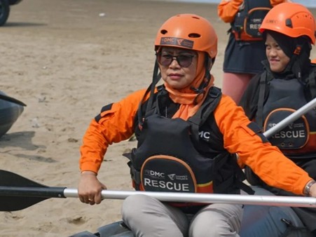 pelatihanbencanadmcdilebak5 dompet dhuafa Rescue team member in an orange helmet and life vest paddling a rescue kayak on a sandy beach, with another rescuer nearby.