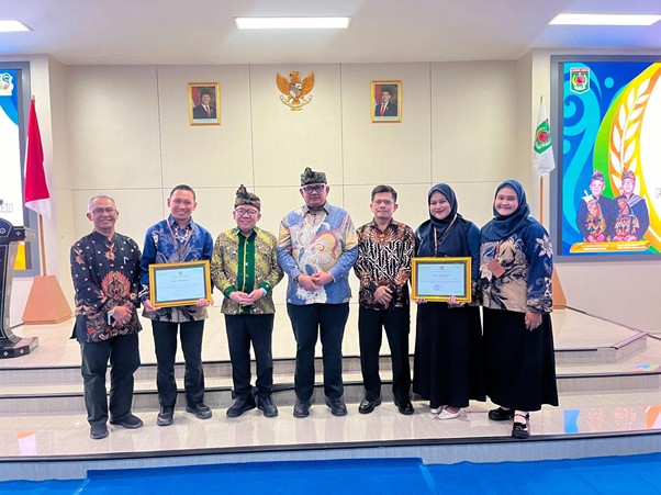 penghargaan untuk bidan untuk negeri 1 dompet dhuafa Group of seven people on a ceremonial stage; two women hold framed certificates while others stand with hands at sides, Indonesian flags and portraits in the background.