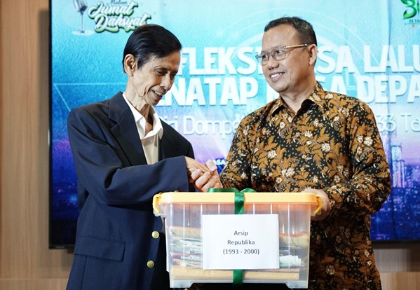 refleksijatidiri13 dompet dhuafa Two men in business attire shake hands over a clear plastic box labeled 'Arsip Republikla (1993-2000)' in front of a blue event backdrop.