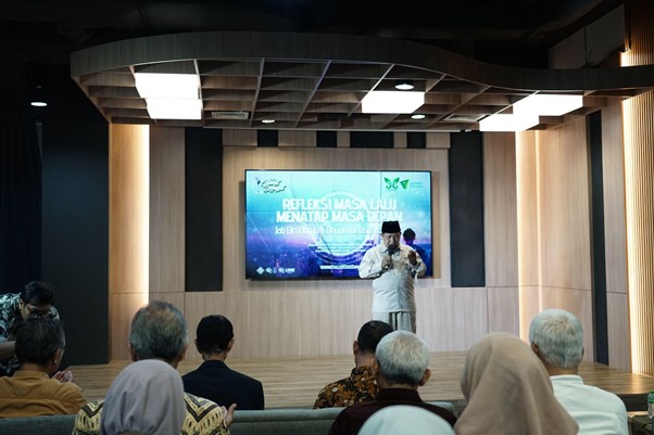 refleksijatidiri16 dompet dhuafa A man on a stage giving a talk to an audience in a modern auditorium with a large screen behind him showing a presentation title.