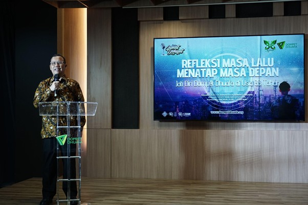 refleksijatidiri5 dompet dhuafa Speaker at a transparent lectern delivers a talk in a conference room, a large presentation screen behind shows a slide with Indonesian title text.
