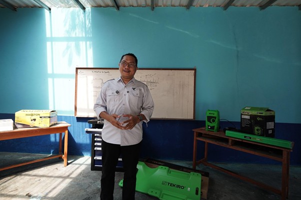 ruang praktikum di smk mitra permata 4 dompet dhuafa Man in a light shirt stands in a workshop beside a whiteboard, with green tool boxes and equipment on tables nearby.