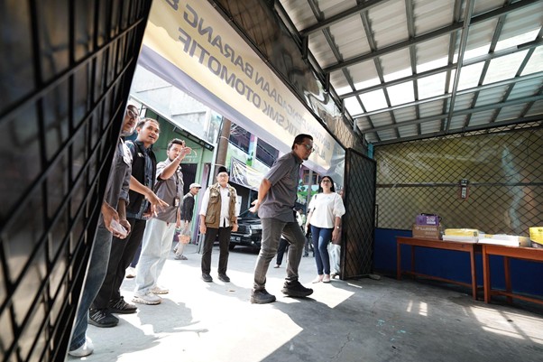 ruang praktikum di smk mitra permata 7 dompet dhuafa A group of people watch as a man steps out through a metal gate into bright daylight.