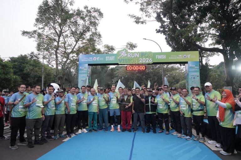 runforvision3768x512 dompet dhuafa Group of participants posing at the start/finish line of a Run for Vision event, all wearing matching green gradient shirts under a bright banner.