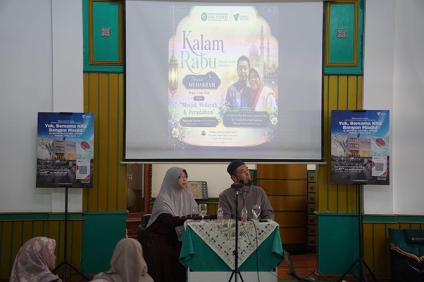 Two speakers sit at a table with a green tablecloth on a stage, a projector screen behind them displays a poster titled 'Kalam Rabbu.'