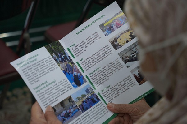 Person holding a tri-fold brochure with photos and text, viewed at an angle.