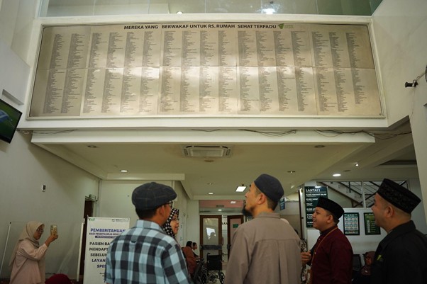 senseisugimotokunjungismart11 dompet dhuafa Group of people in a lobby looking up at a large wall-mounted plaque listing many names.
